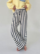 Person wearing a yellow sweater and black and white striped pants on a plain background