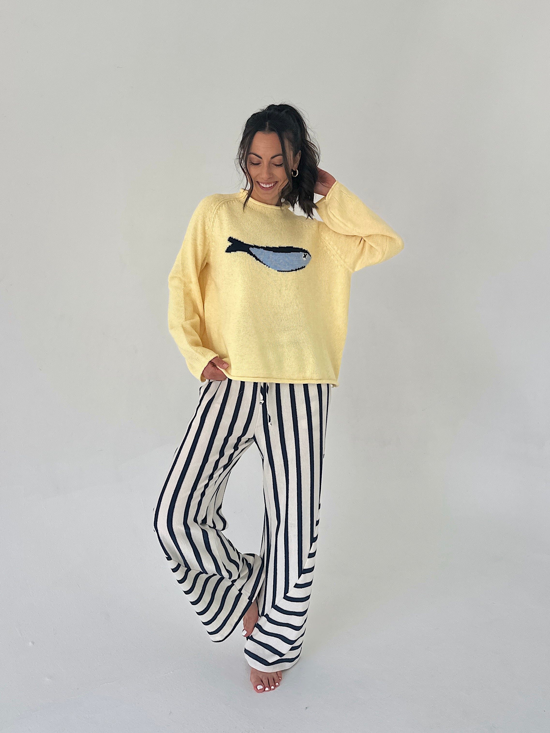 Person wearing a yellow sweater with a fish design and black and white striped pants on a plain background