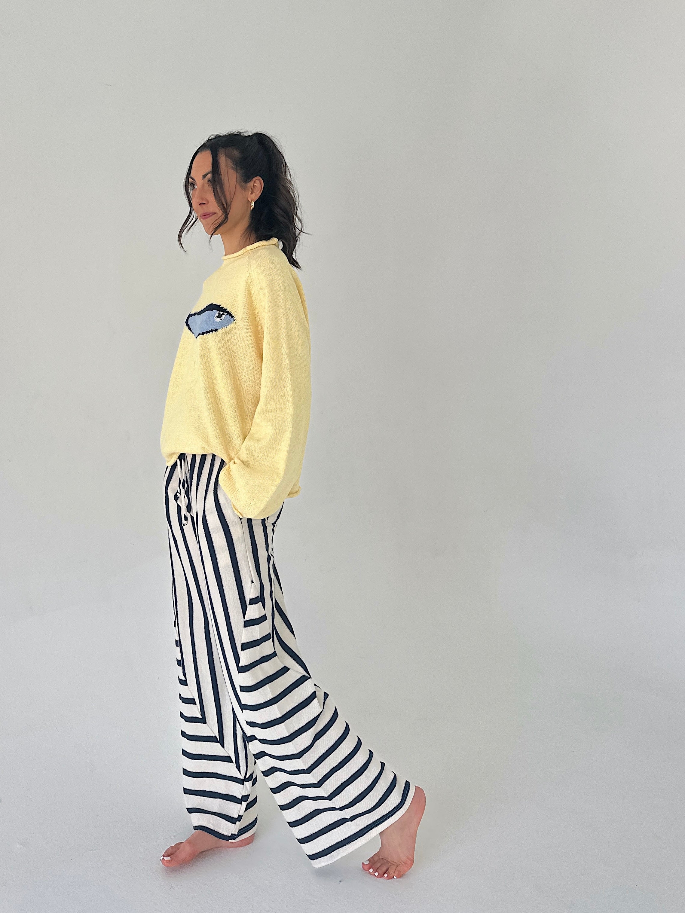 Person wearing a yellow sweater and black and white striped pants on a plain background