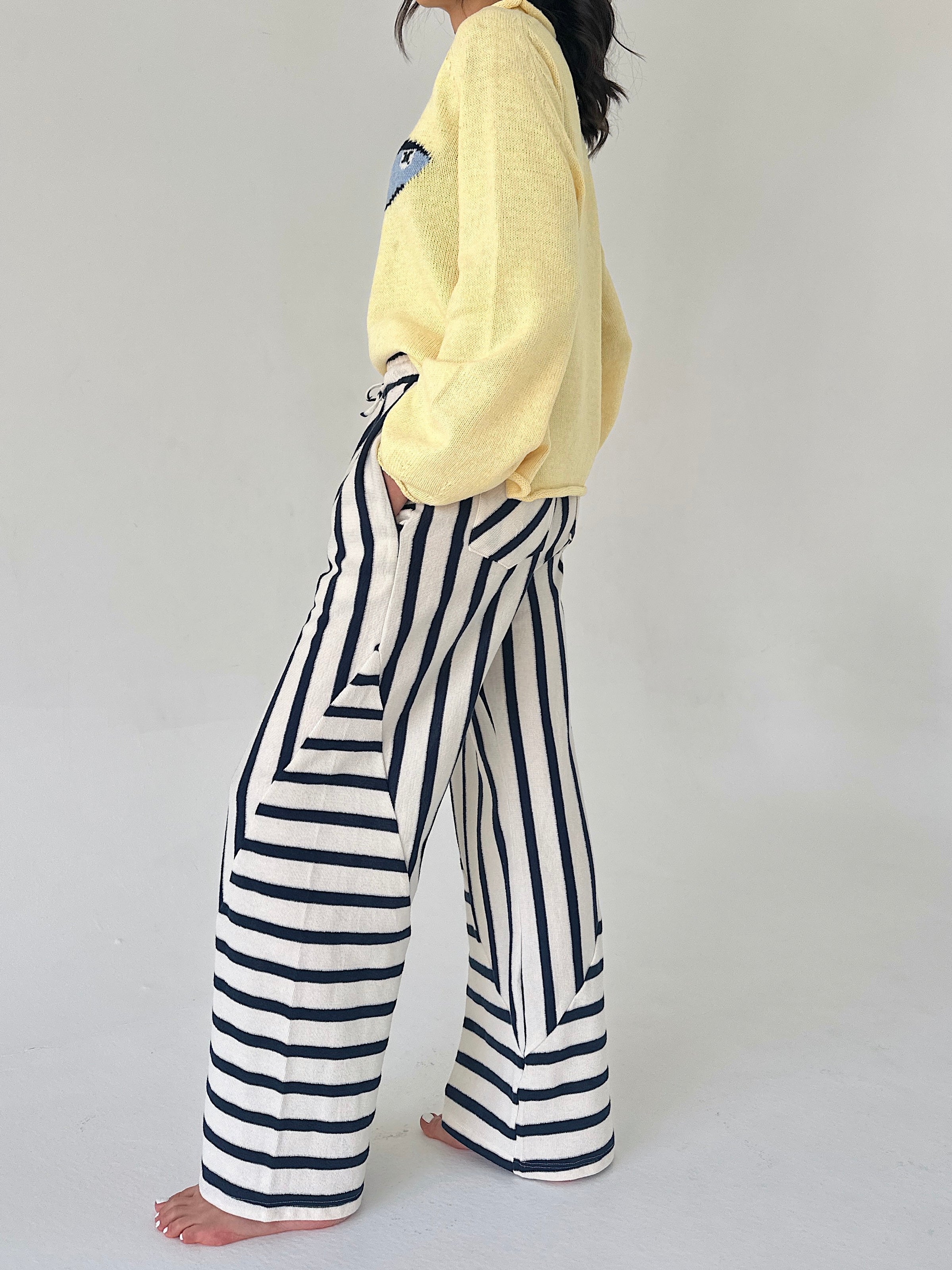 Person wearing a yellow sweater and black and white striped pants on a plain background from side