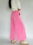 Person wearing pink wide-leg pants and a white top on a plain background showing back