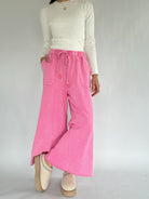 Person wearing a white long-sleeve top and pink wide-leg pants on a plain background