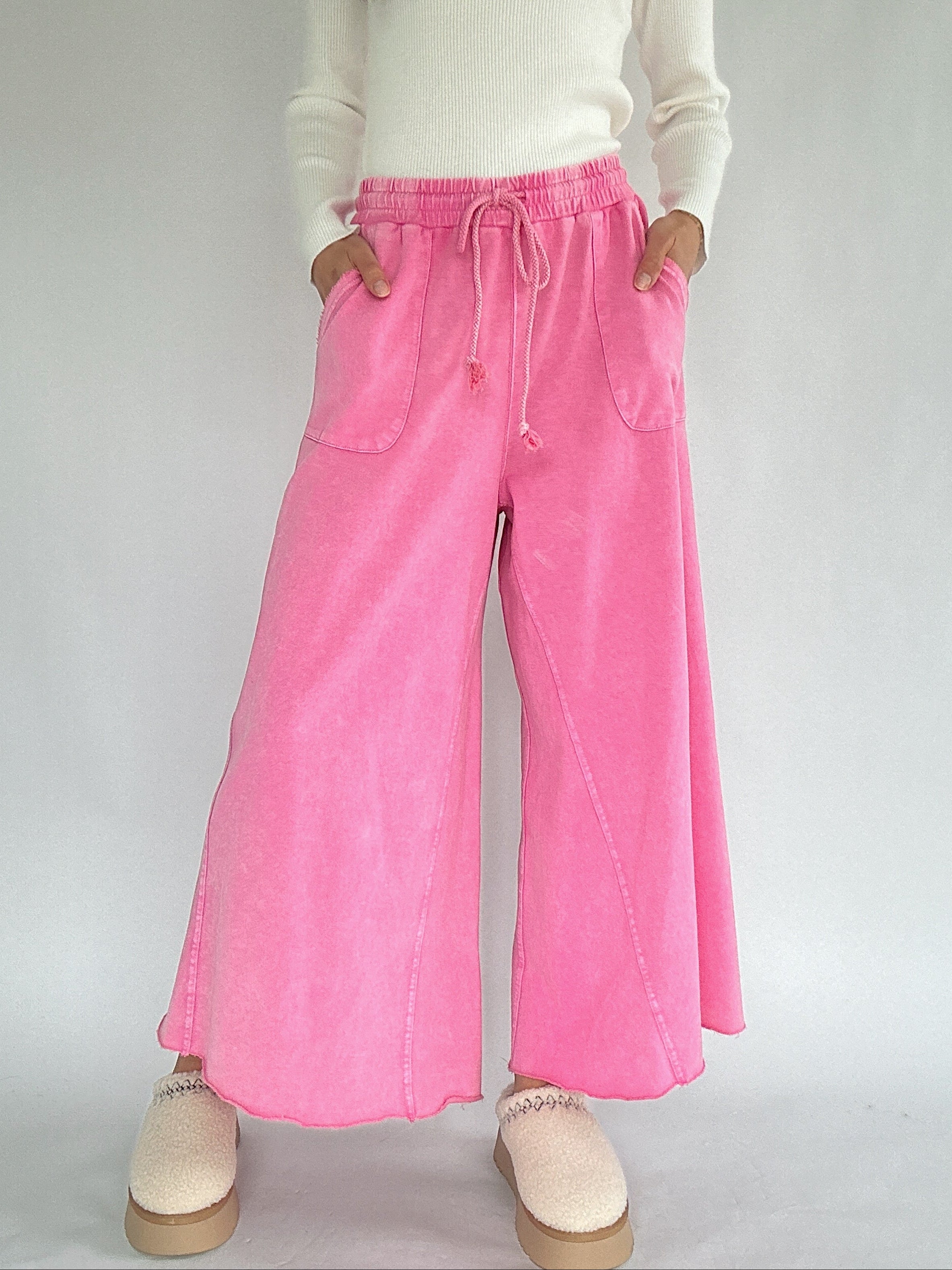 Person wearing pink wide leg sweatpants and a white top on a plain background