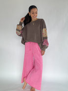 Woman wearing a brown sweatshirt with colorful sleeves and pink wide leg sweatpants on a white background