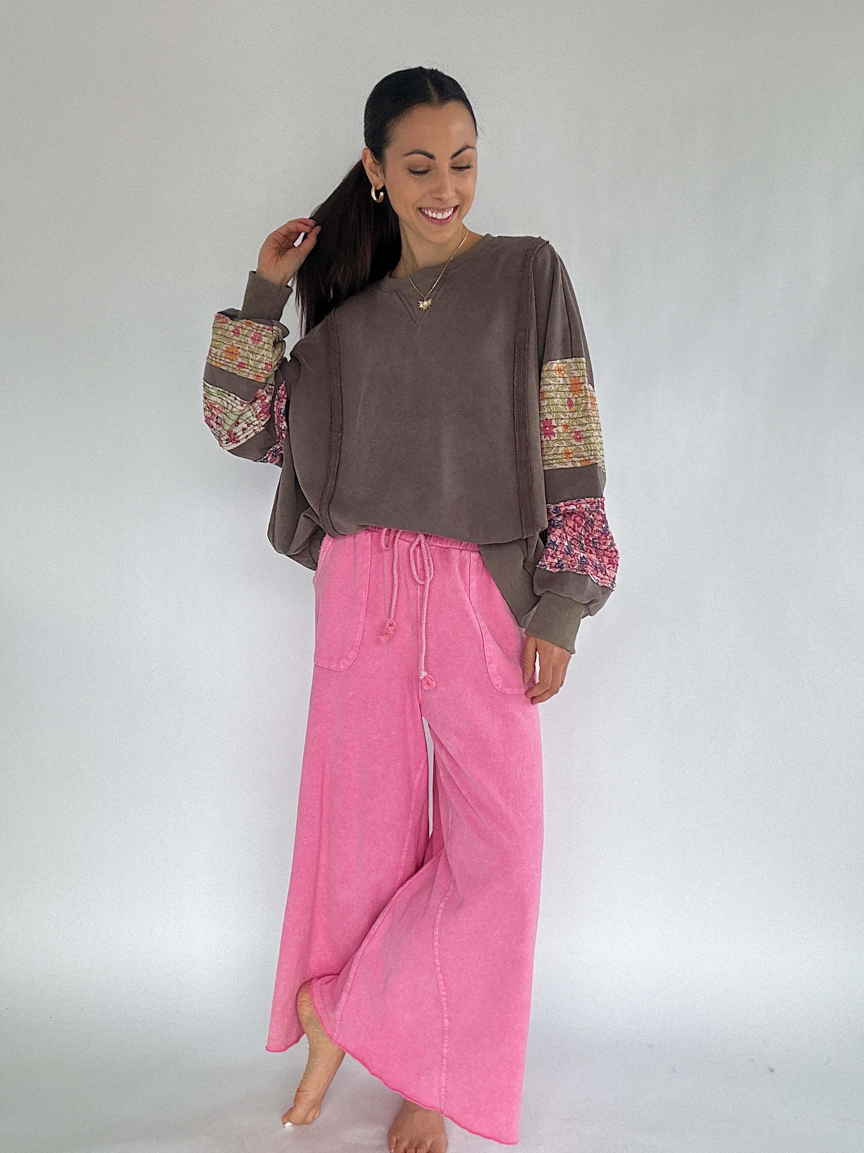 Woman wearing a brown sweatshirt with colorful sleeves and pink wide leg sweatpants on a white background