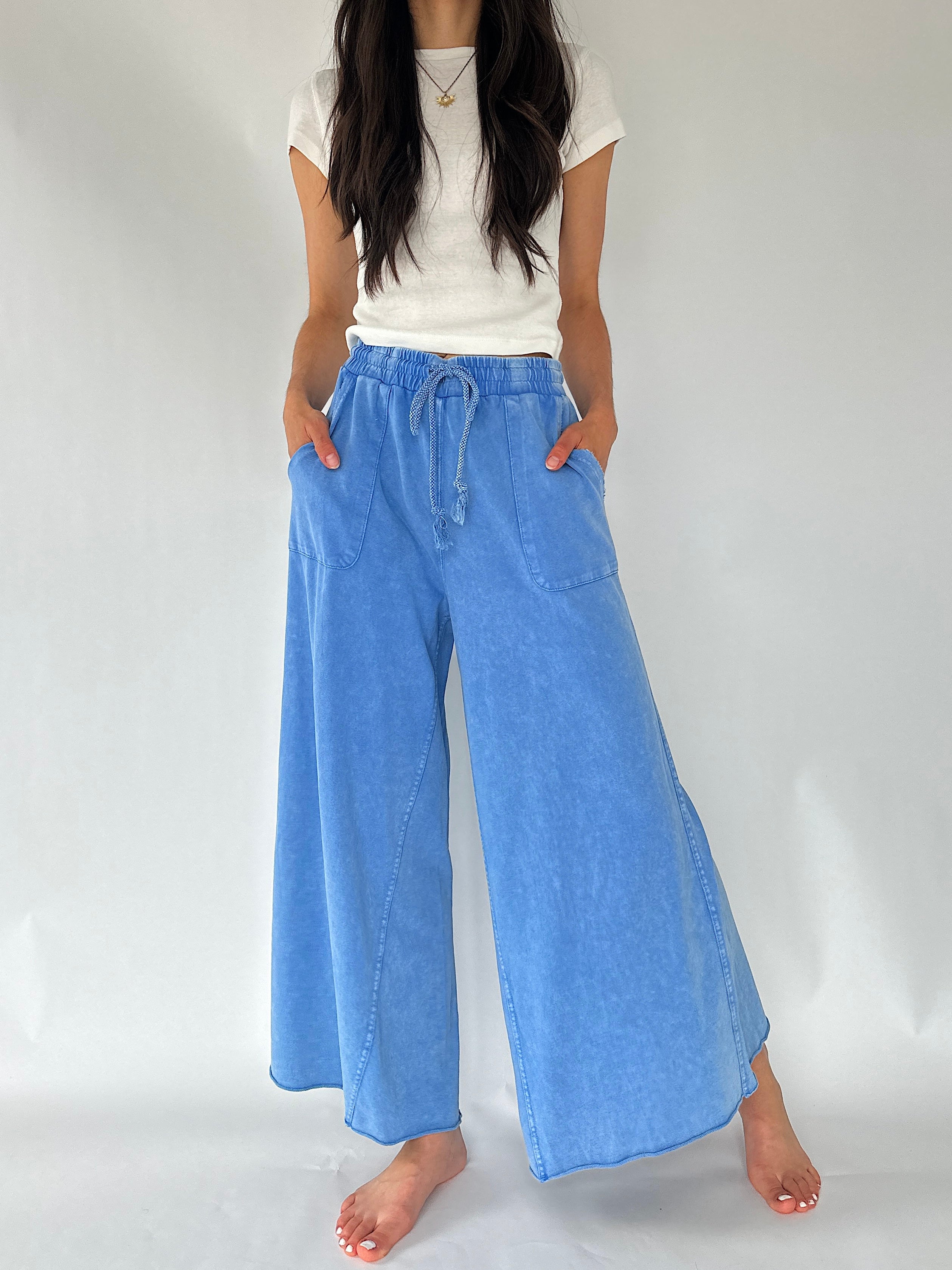 A model wearing light blue wide-leg pants with a drawstring waistband, paired with a white t-shirt, shown against a plain light gray studio background.