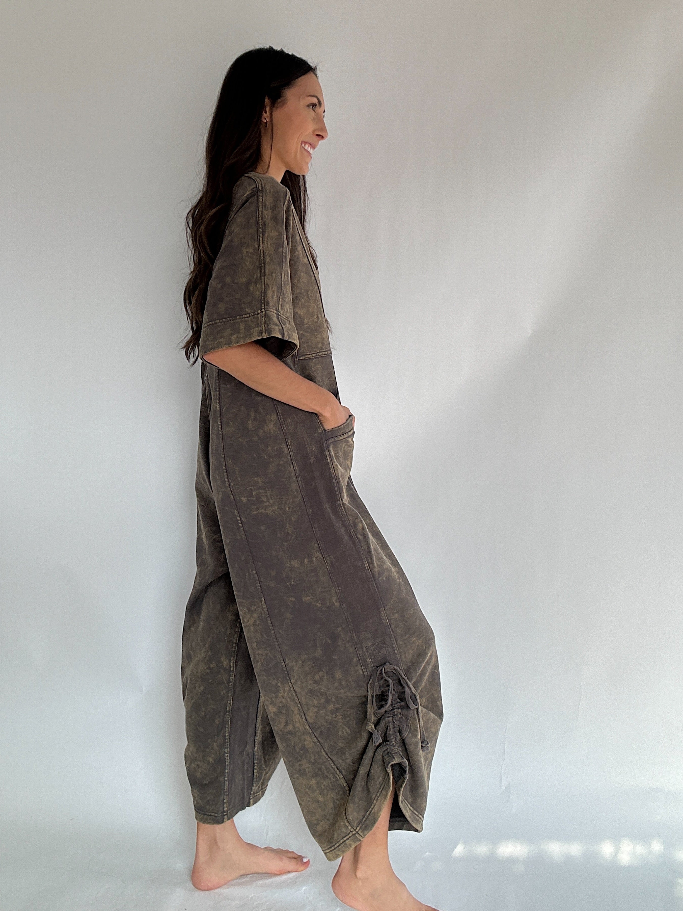 Woman wearing a brown jumpsuit against a white background to show side view