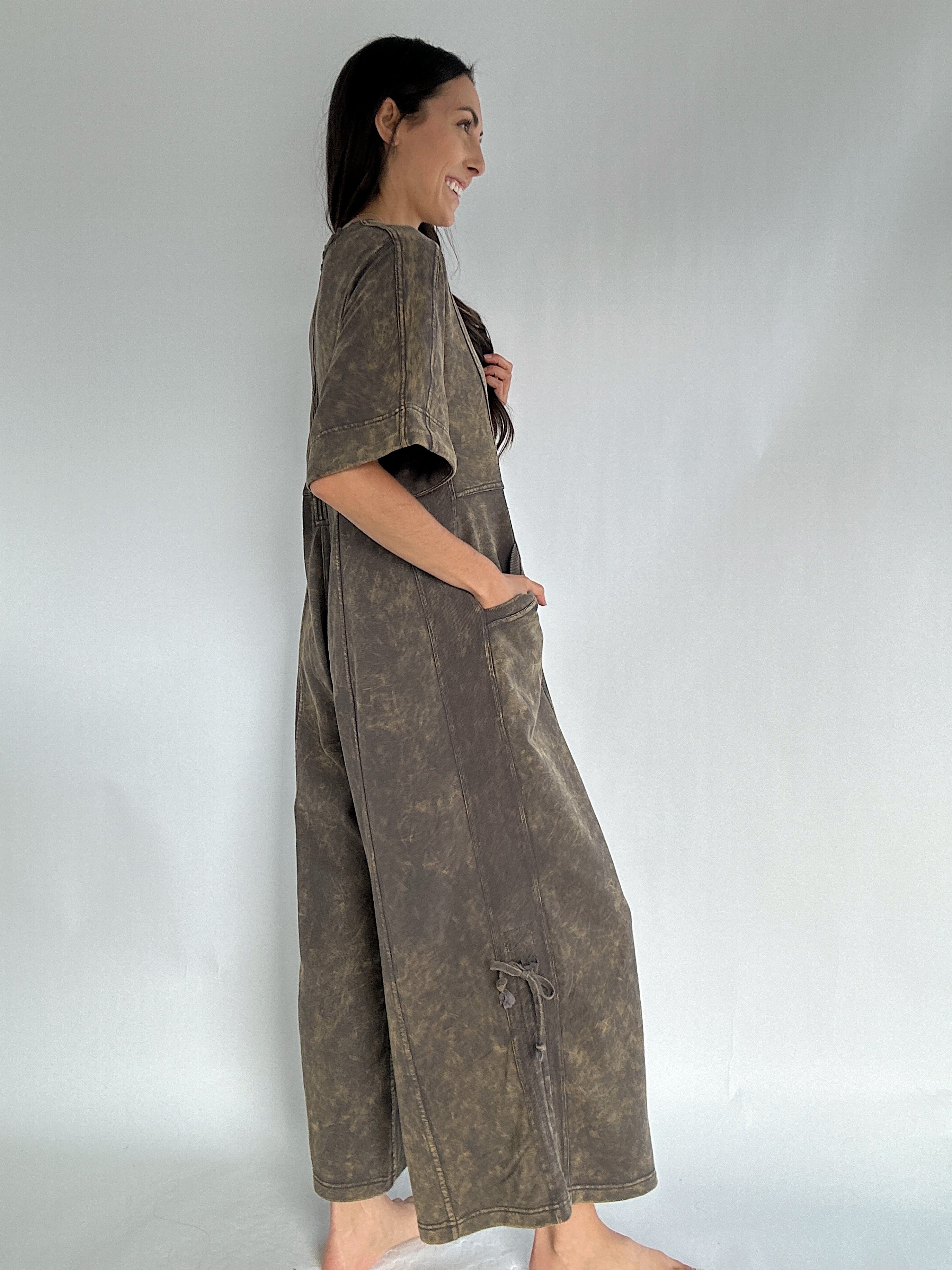 Woman wearing a brown jumpsuit against a plain background to show side view with ties let loose