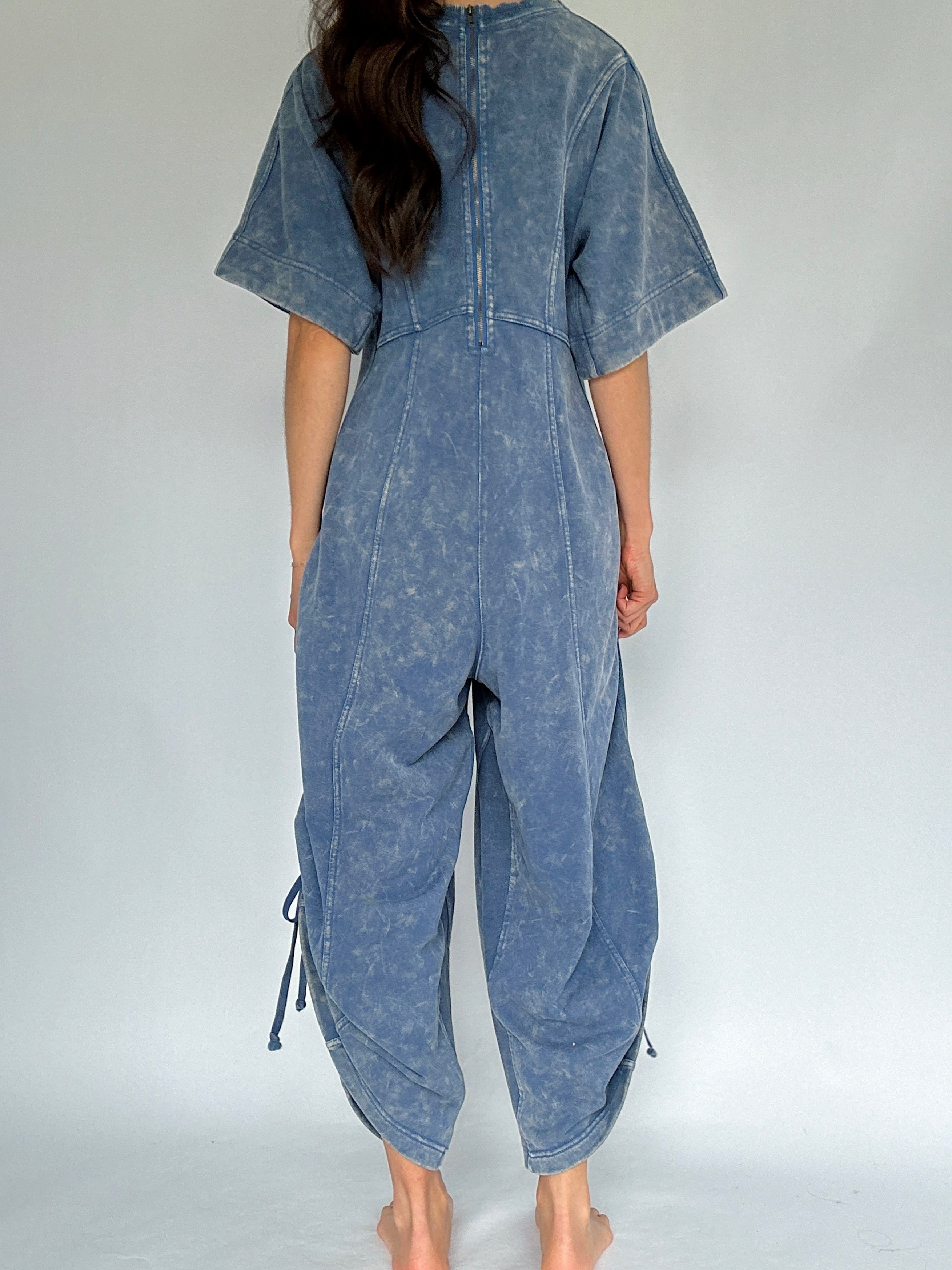 Person wearing a blue mineral-wash jumpsuit on a white background to show back view