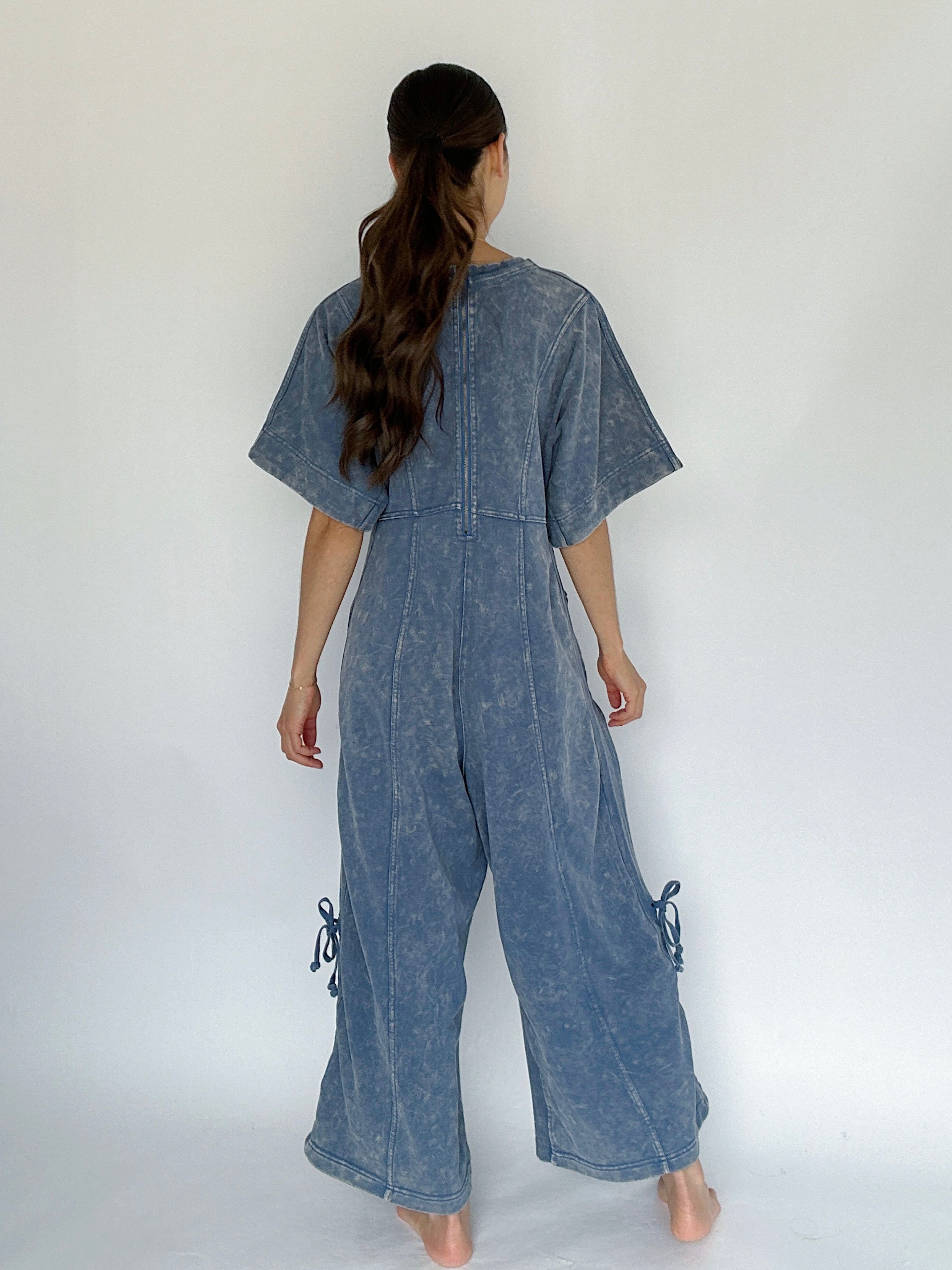 Woman wearing a blue denim jumpsuit against a white background to show back view