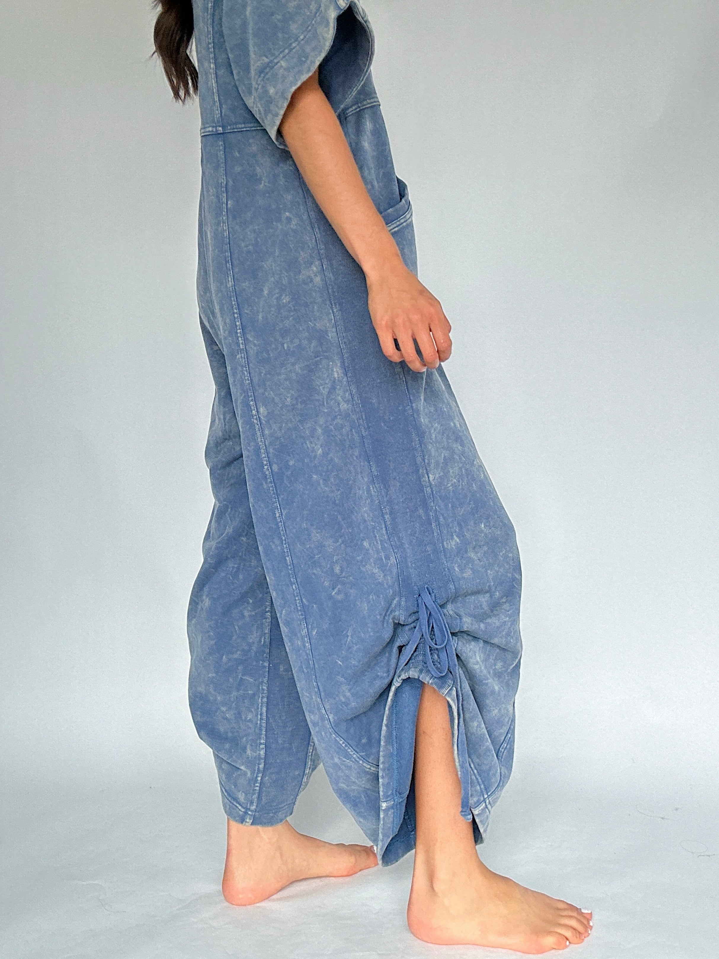 Person wearing a blue jumpsuit with cinched up sides on a plain background