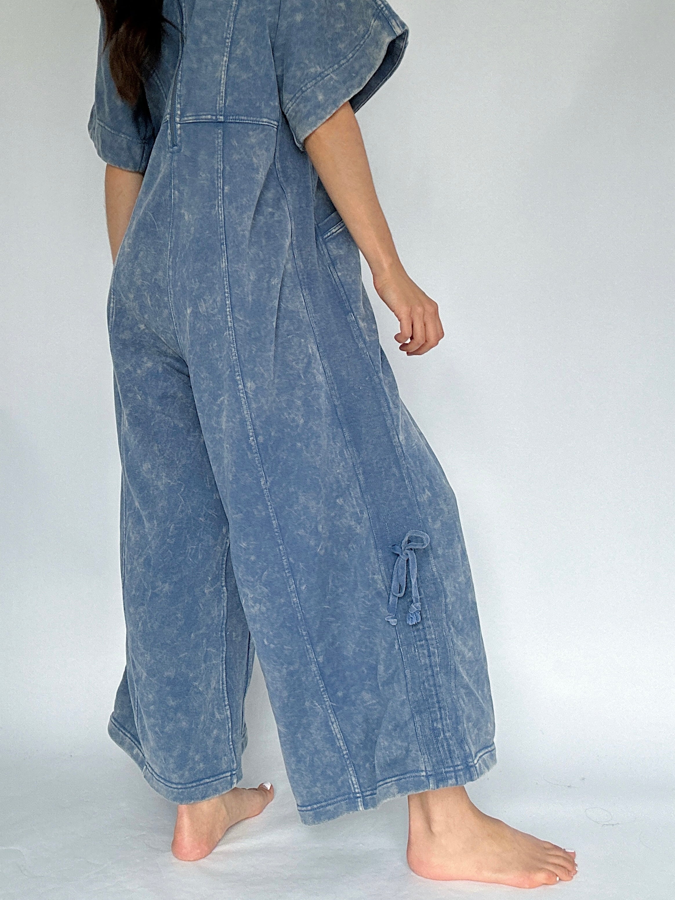 Person wearing a blue acid-wash jumpsuit on a white background to show side tie detail