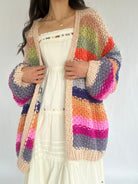 Multicolored striped cardigan worn over a white dress on a plain background