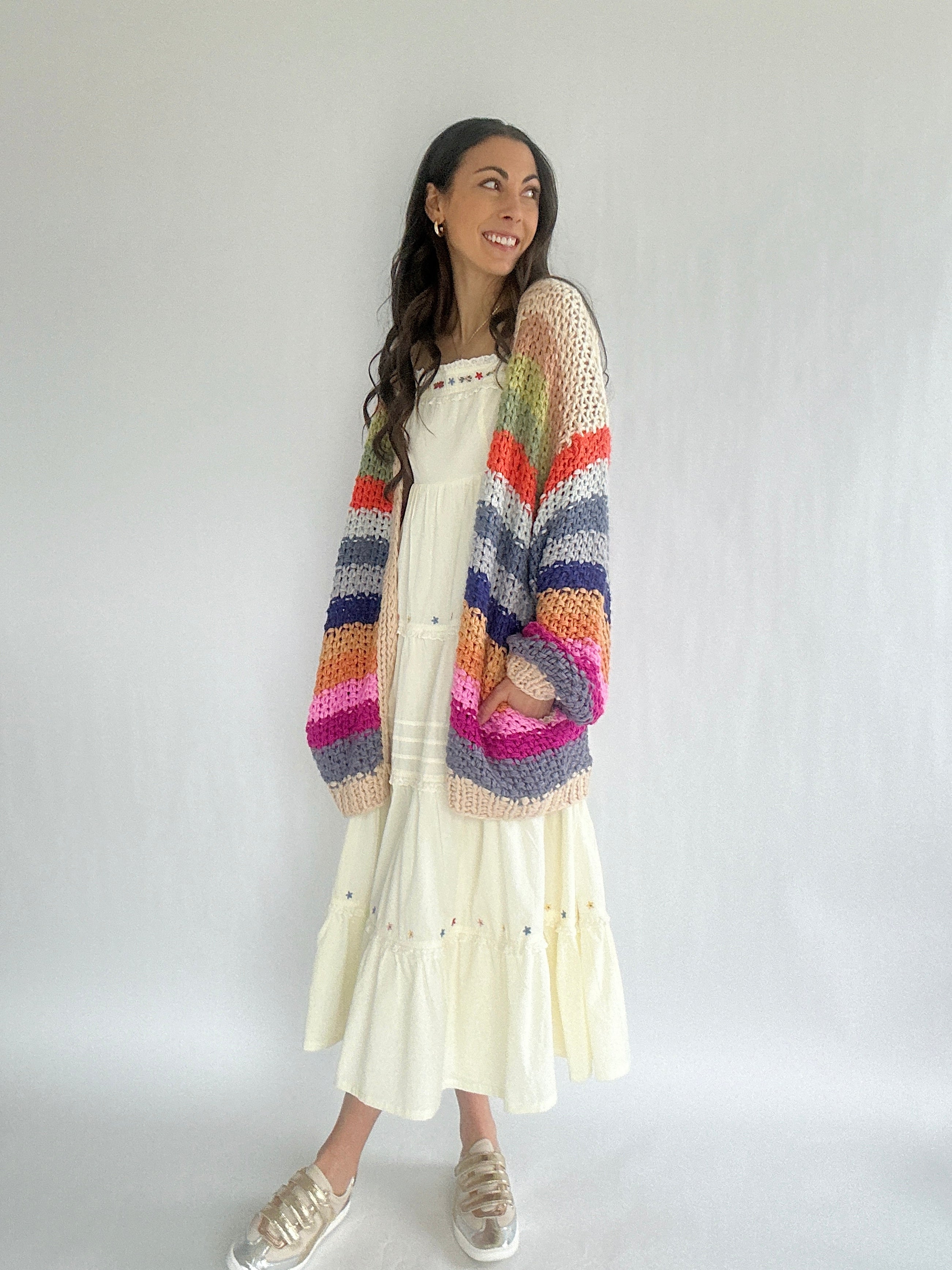 Woman wearing a colorful striped cardigan over a white dress on a plain background
