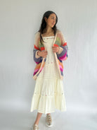 Woman wearing a colorful cardigan over a white dress on a plain background