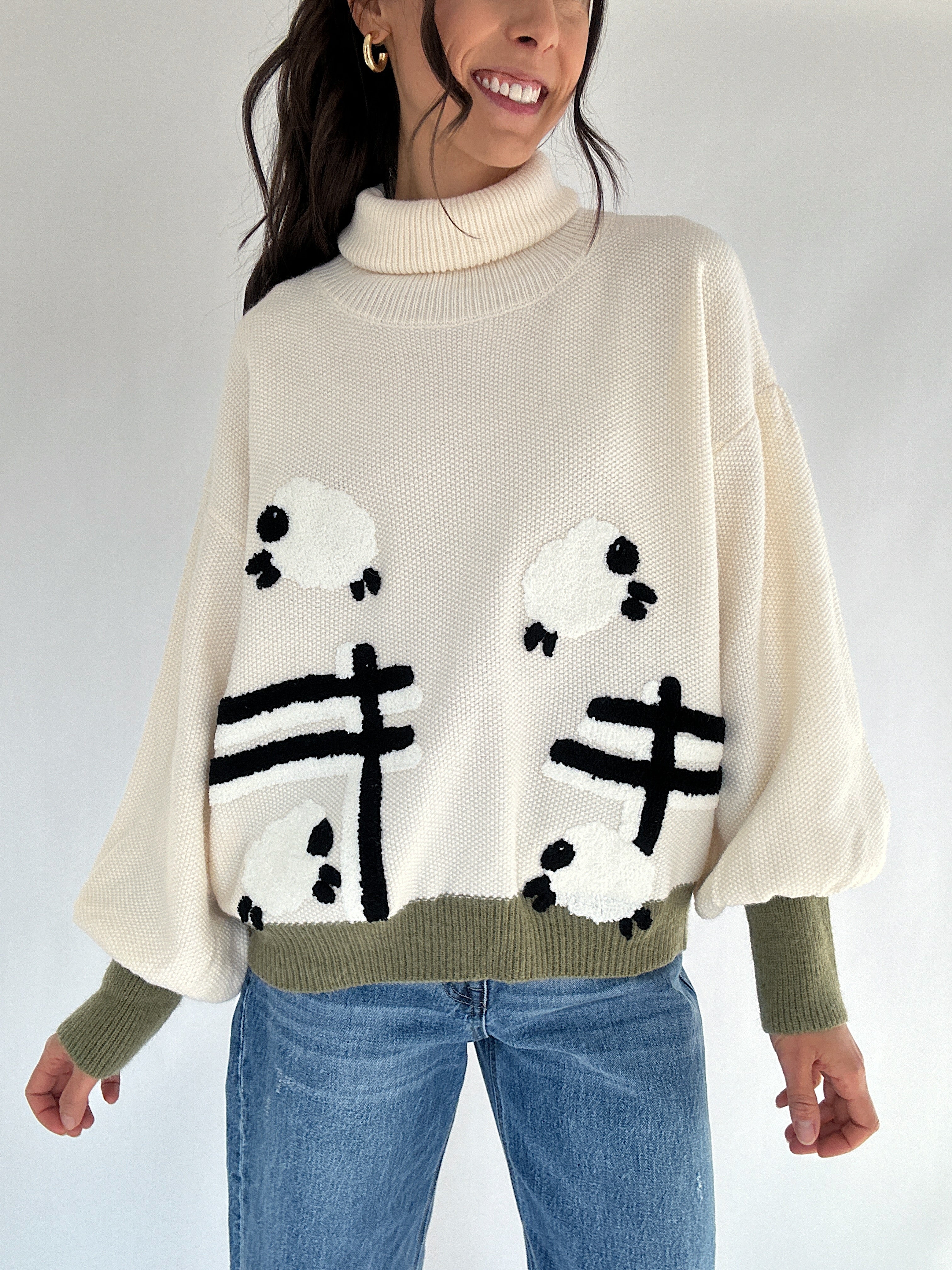 Person wearing a cream turtle neck sweater with sheep jumping over a fence designs on a plain background