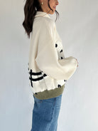 Person wearing a cream turtle neck sweater with graphic patterns and blue jeans on a plain background showing side