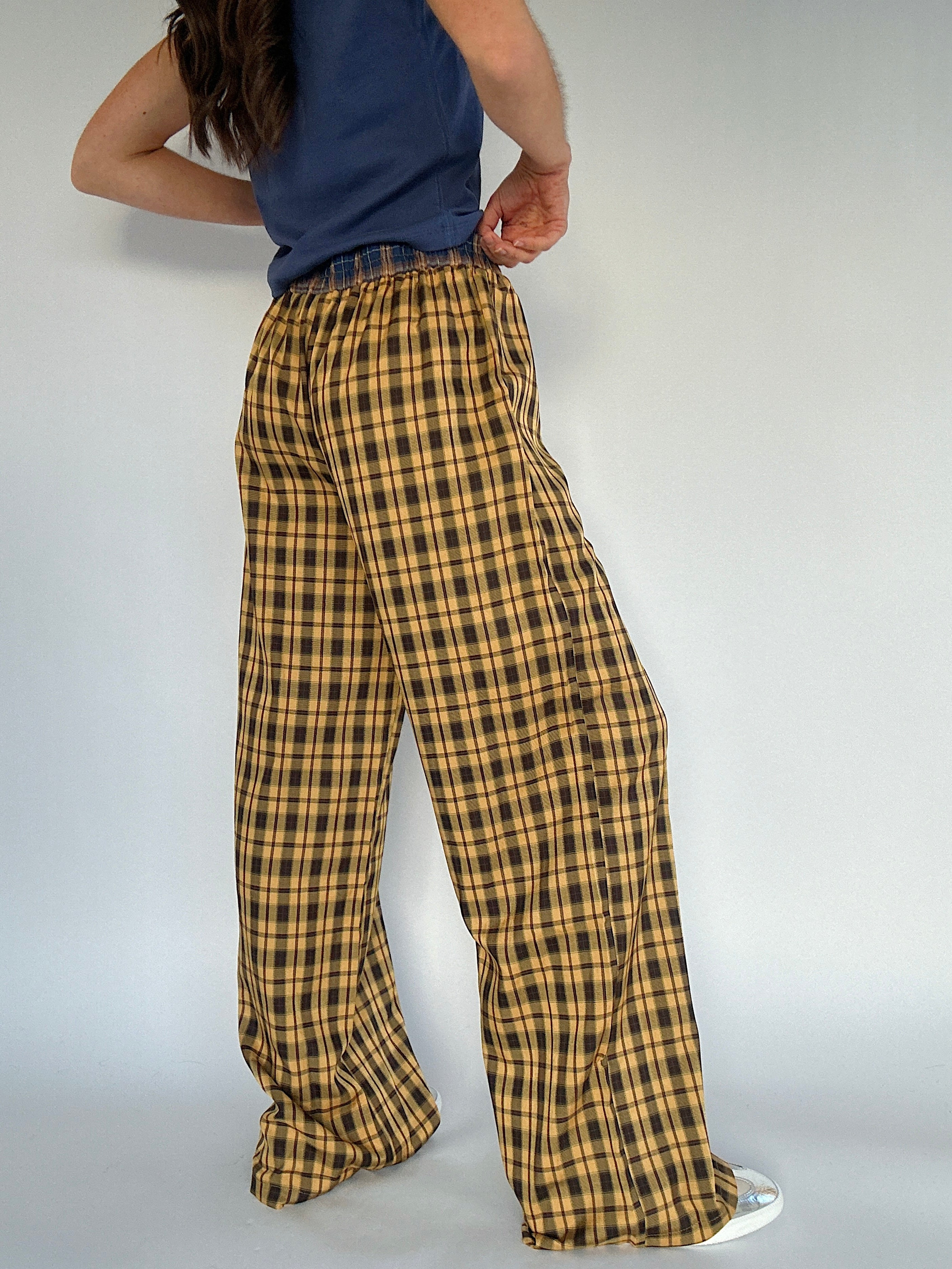 Person wearing yellow plaid pants and a blue top on a plain background showing the back