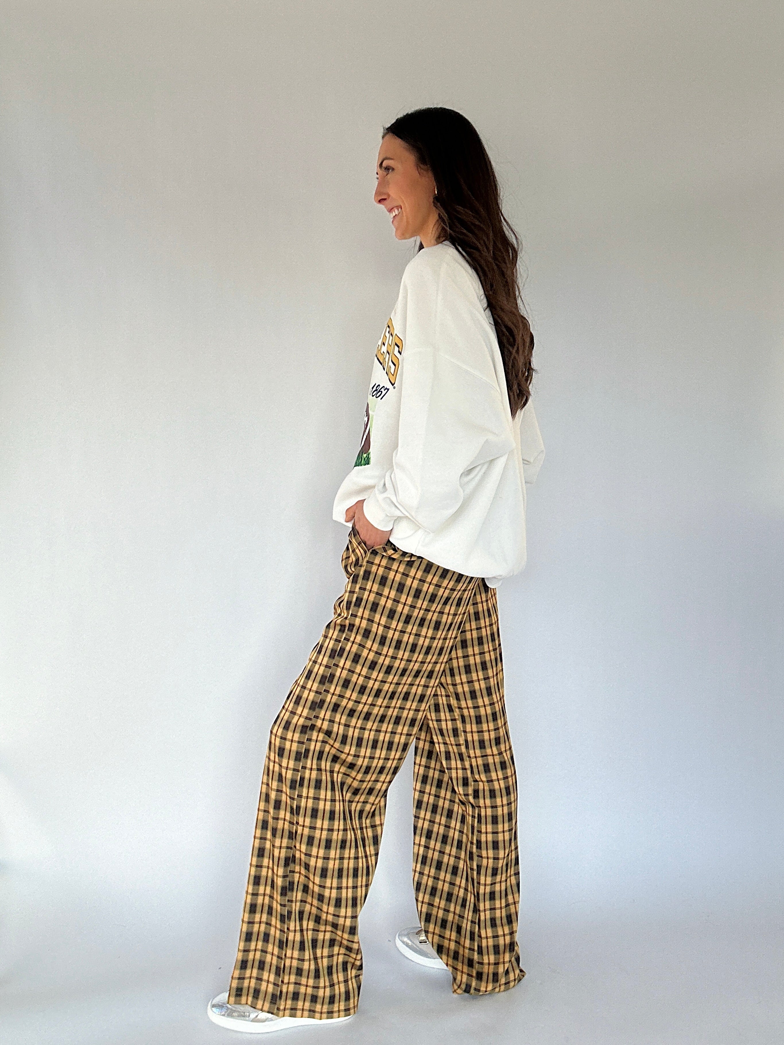 Woman wearing a white sweatshirt and plaid pants against a plain background showing side view