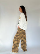 Woman wearing a white sweatshirt and plaid pants against a plain background showing side view