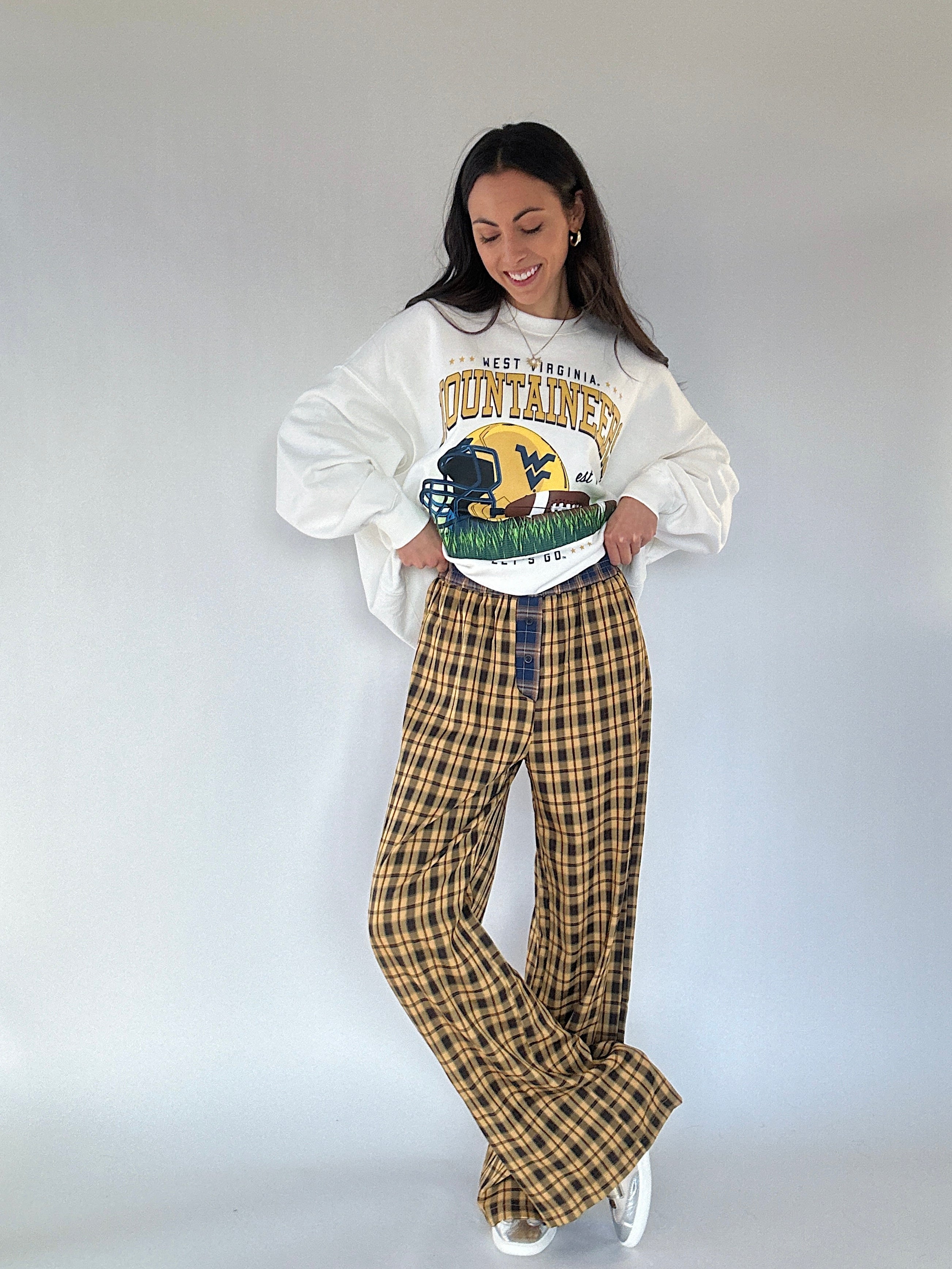 Person wearing a West Virginia Mountaineers sweatshirt and plaid pants on a plain background