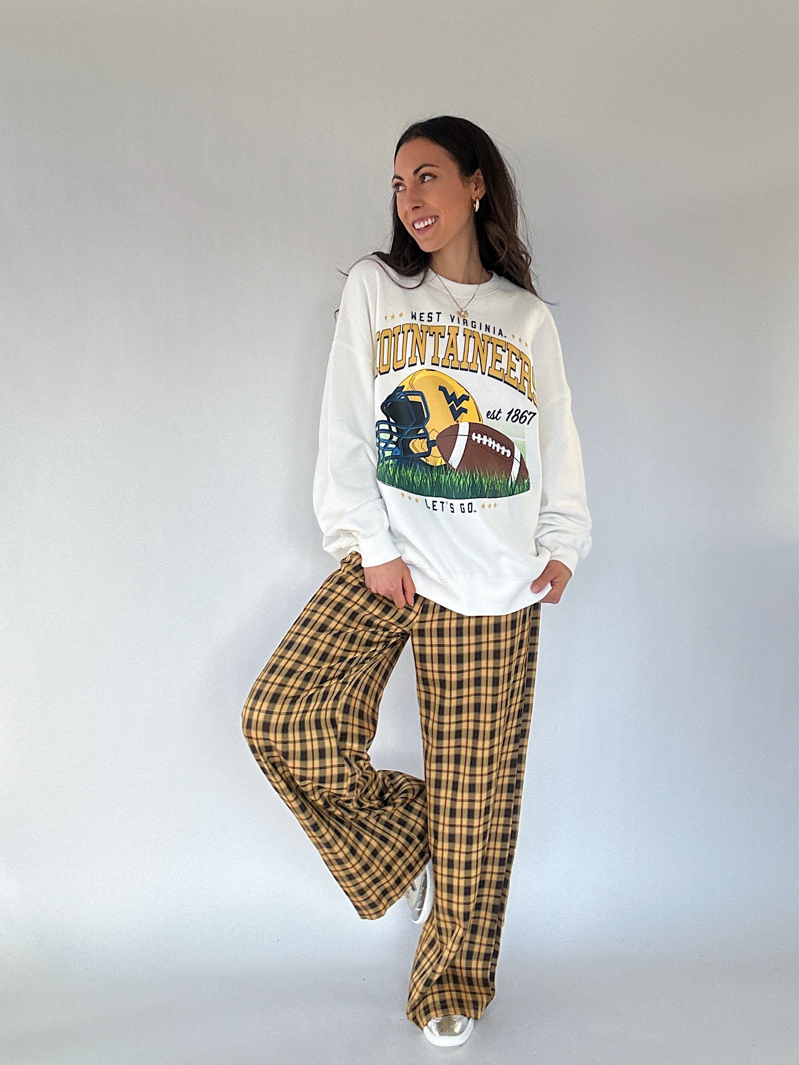 Woman wearing a 'West Virginia Mountaineers' sweatshirt and plaid pants against a white background