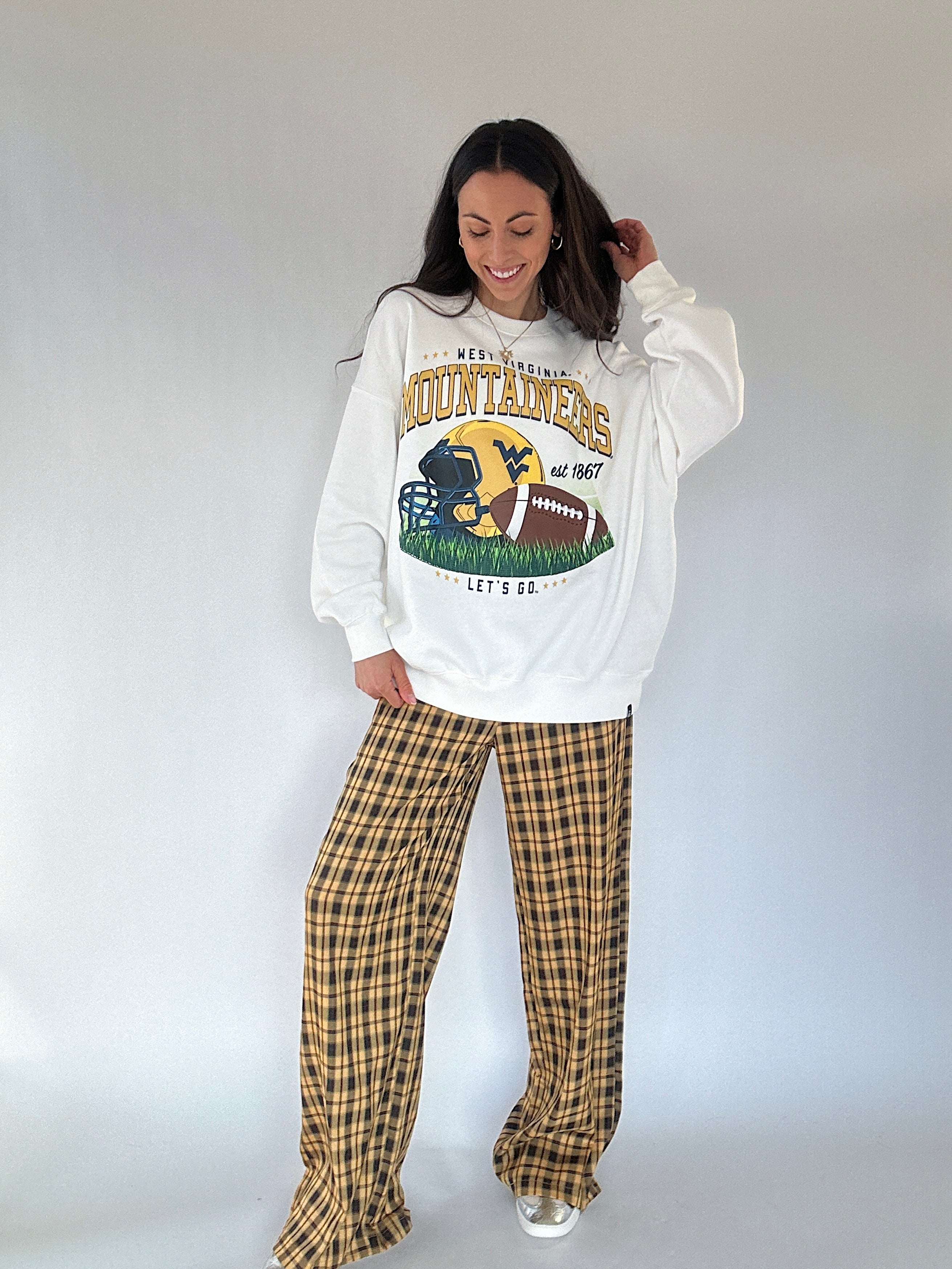 Person wearing a white WV Mountaineers sweatshirt and yellow plaid pants on a plain background