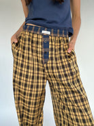Person wearing mustard yellow plaid pants with a blue shirt on a plain background showing blue plaid waistband and side pockets