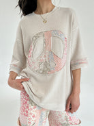 Person wearing a beige thermal knit top with a peace symbol design on a white background