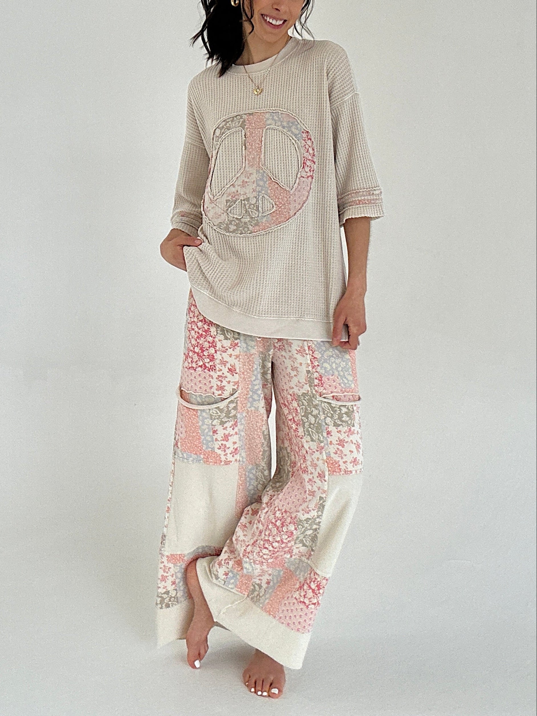 Woman wearing a beige top with a peace symbol and patterned pants on a white background