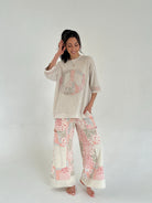 Woman wearing a beige peace sign top and floral pants on a white background