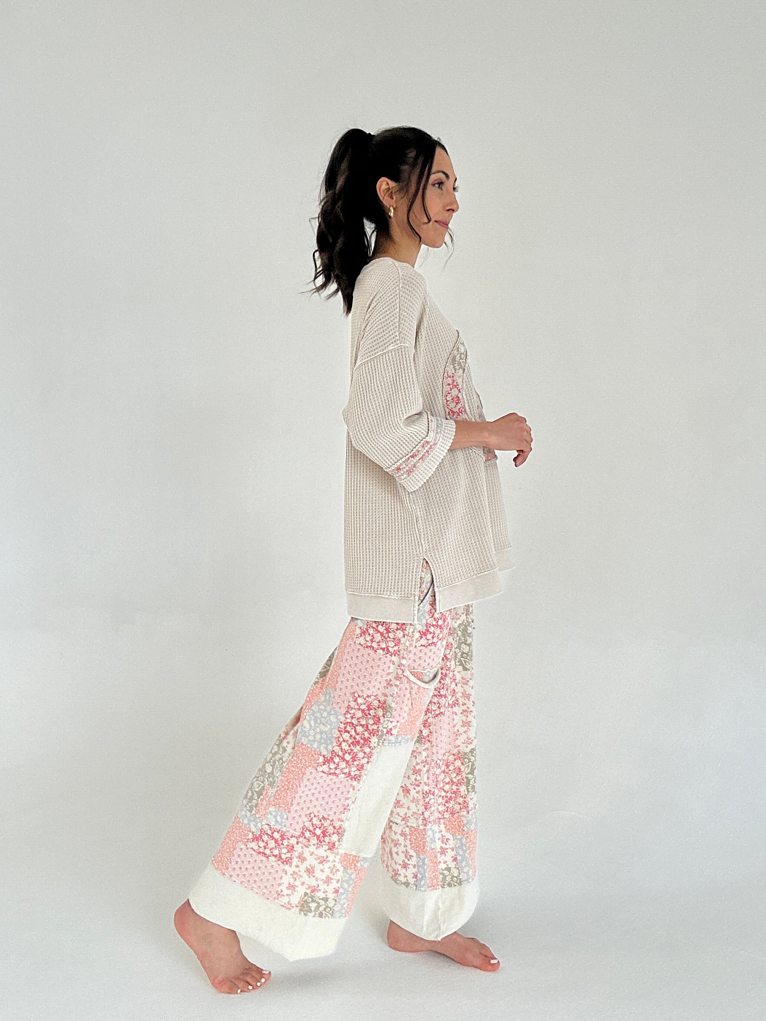 Woman wearing a cream knit top and floral pants on a white background