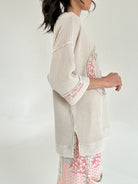 Person wearing a textured beige top with floral patterns on a plain background