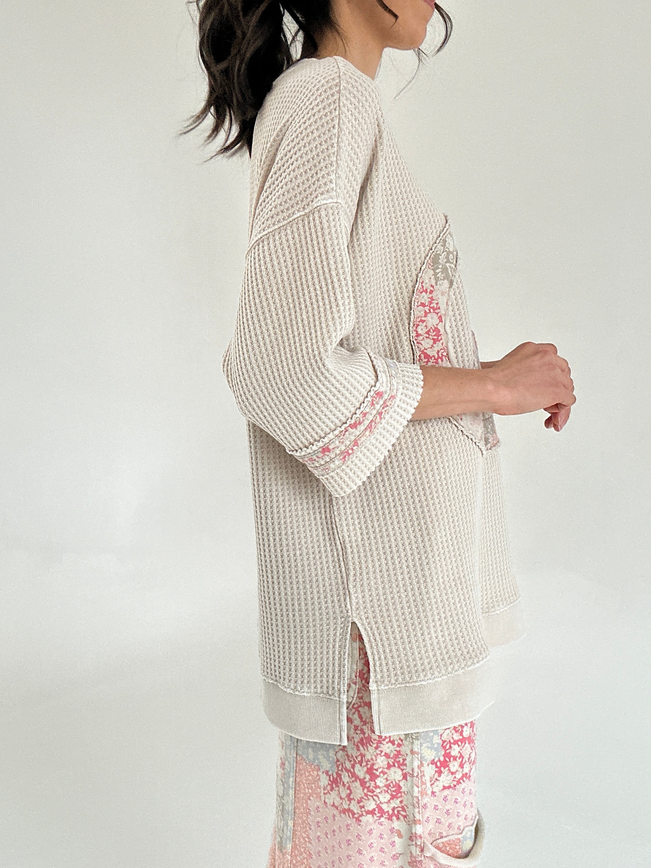 Person wearing a textured beige top with floral patterns on a plain background