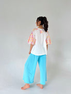 Person wearing a white top with colorful plaid sleeves and light blue pants on a plain background
