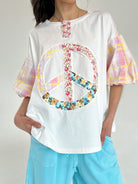 Person wearing a white t-shirt with a colorful peace sign symbol design on a plain background