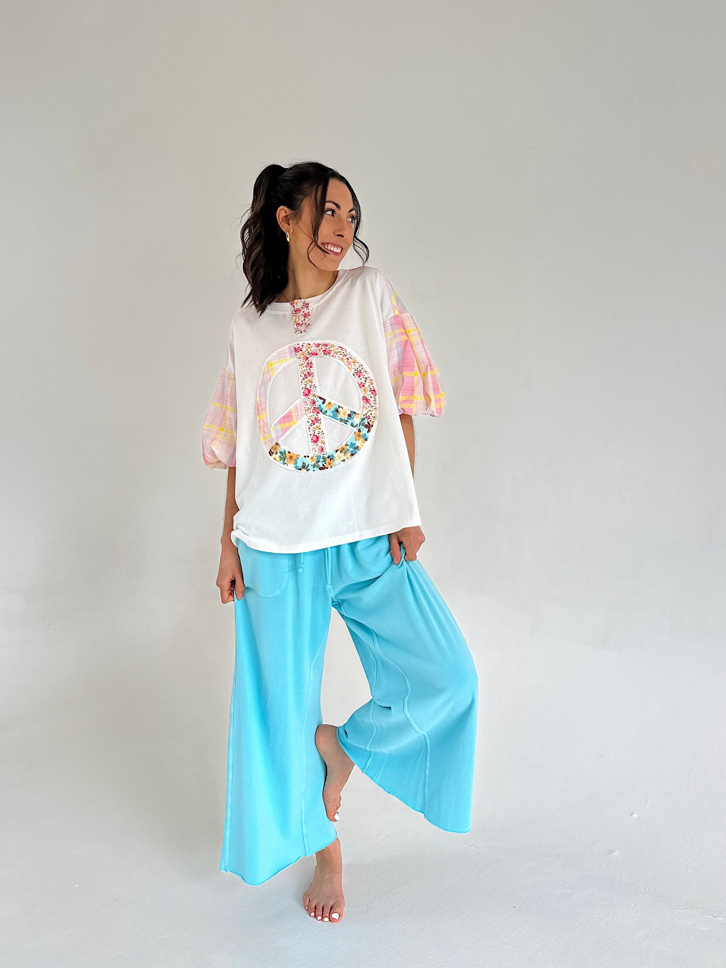 Woman wearing a white t-shirt with colorful peace sign design and light blue pants on a plain background
