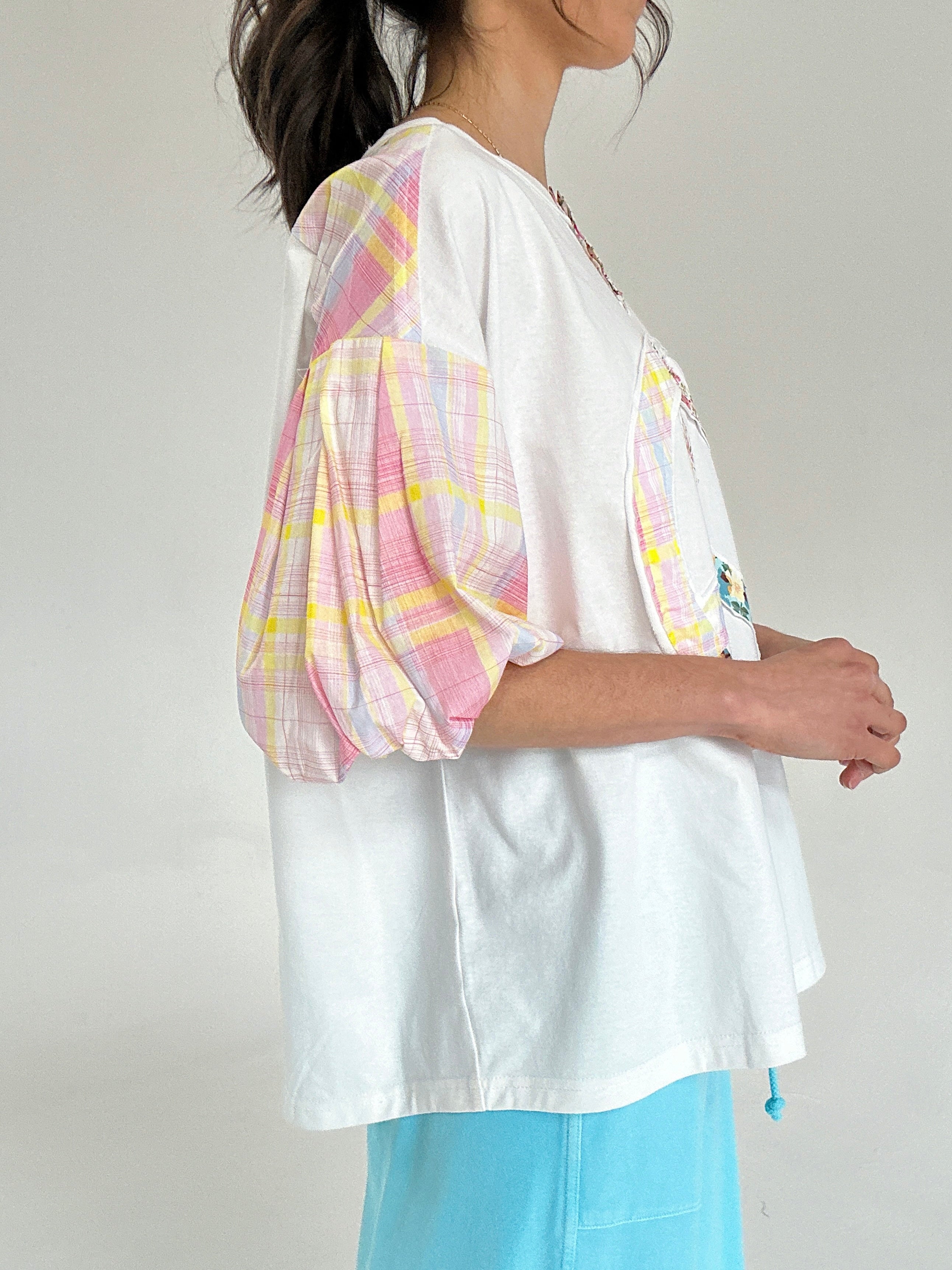 Woman wearing a white tee with colorful plaid sleeves and light blue pants on a plain background showing side
