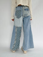 Person wearing unique denim pants with patchwork design on a plain background showing the back details