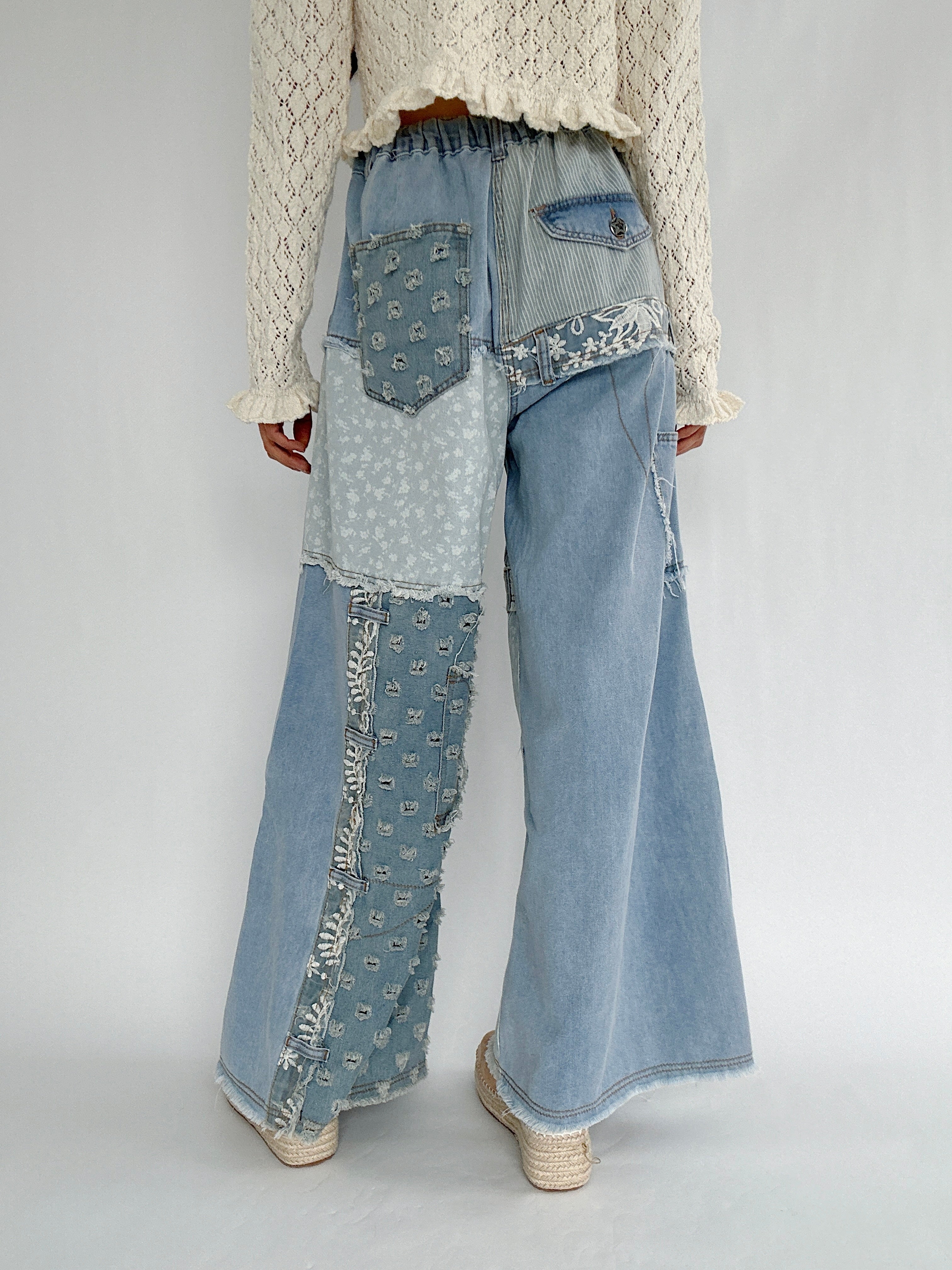 Person wearing unique denim pants with patchwork design on a plain background showing the back details