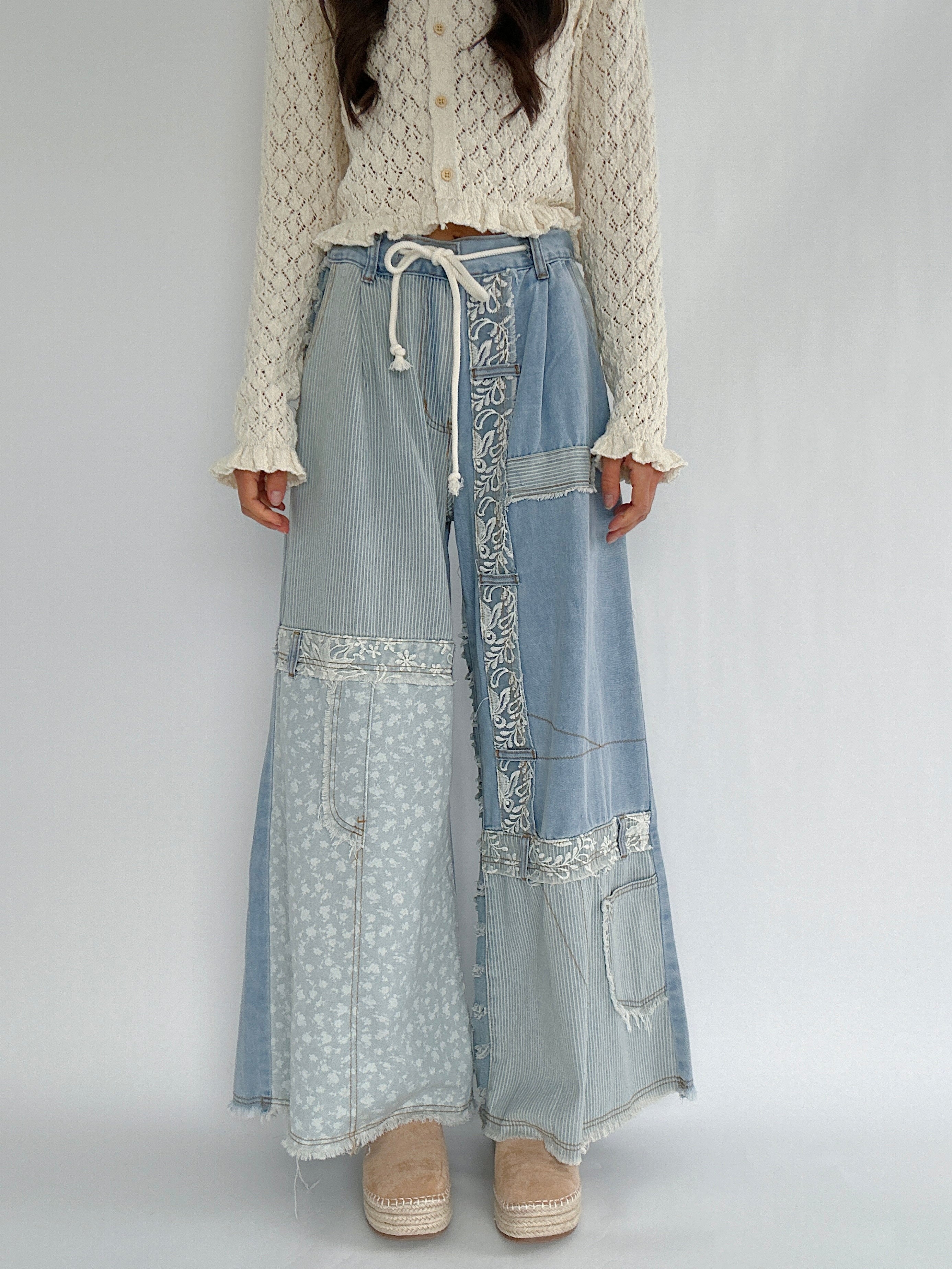 Person wearing wide leg denim pants with patchwork details on a plain background