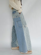 Person wearing denim patchwork pants with floral patterns on a plain background showing the side