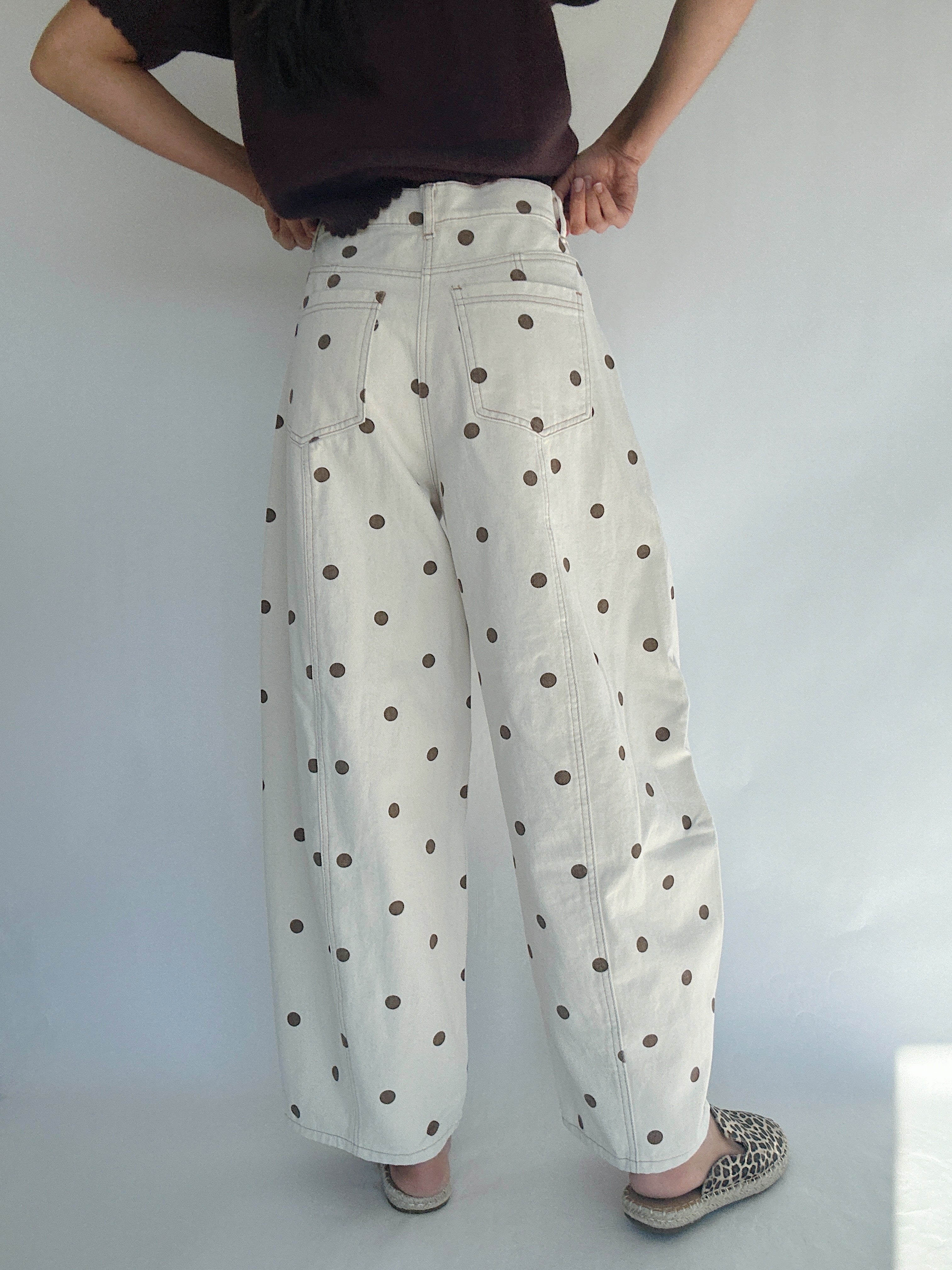 Person wearing white barrel style pants with brown polka dots against a plain background back view