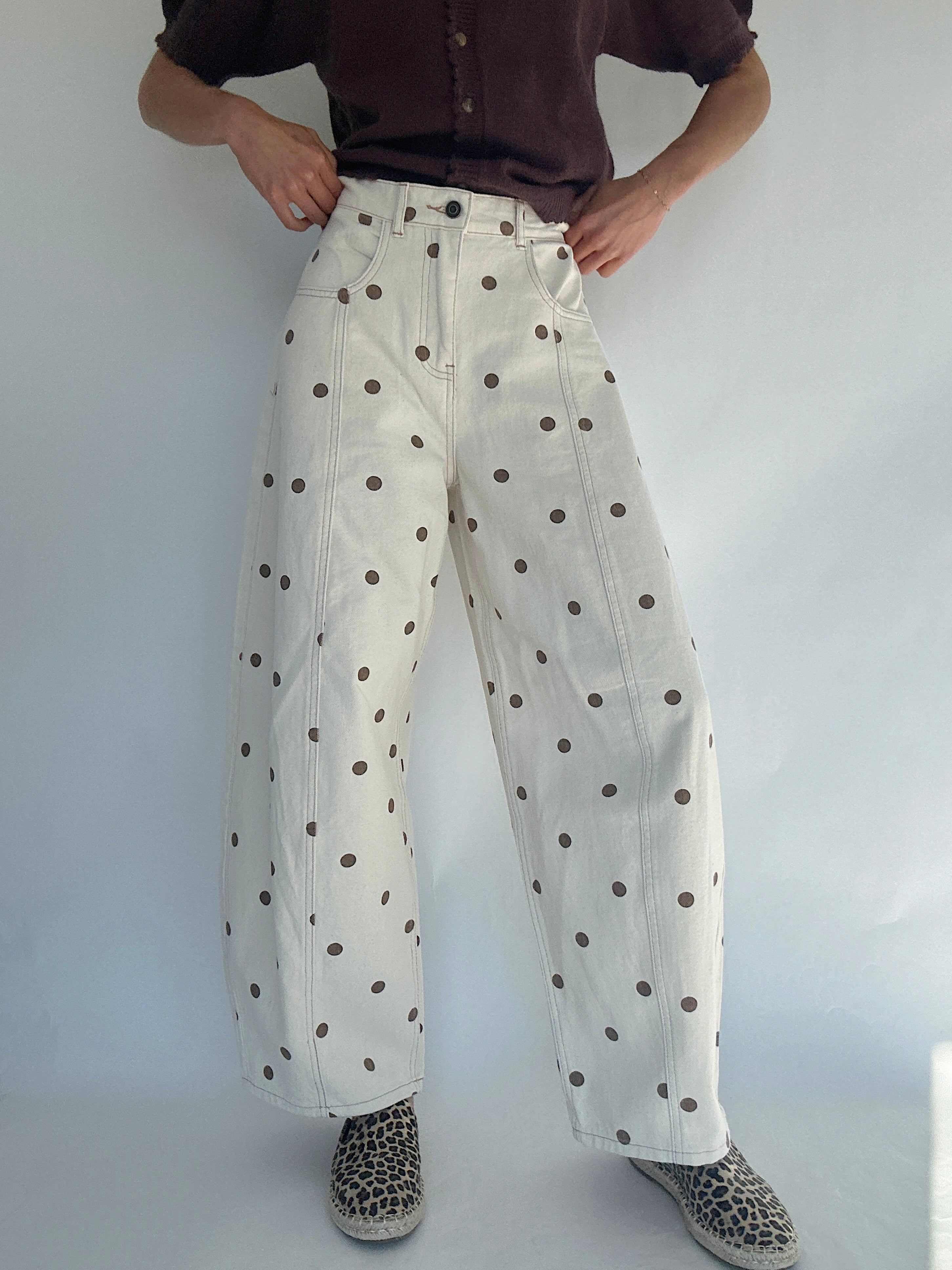 Person wearing white barrel style pants with brown polka dots against a plain background