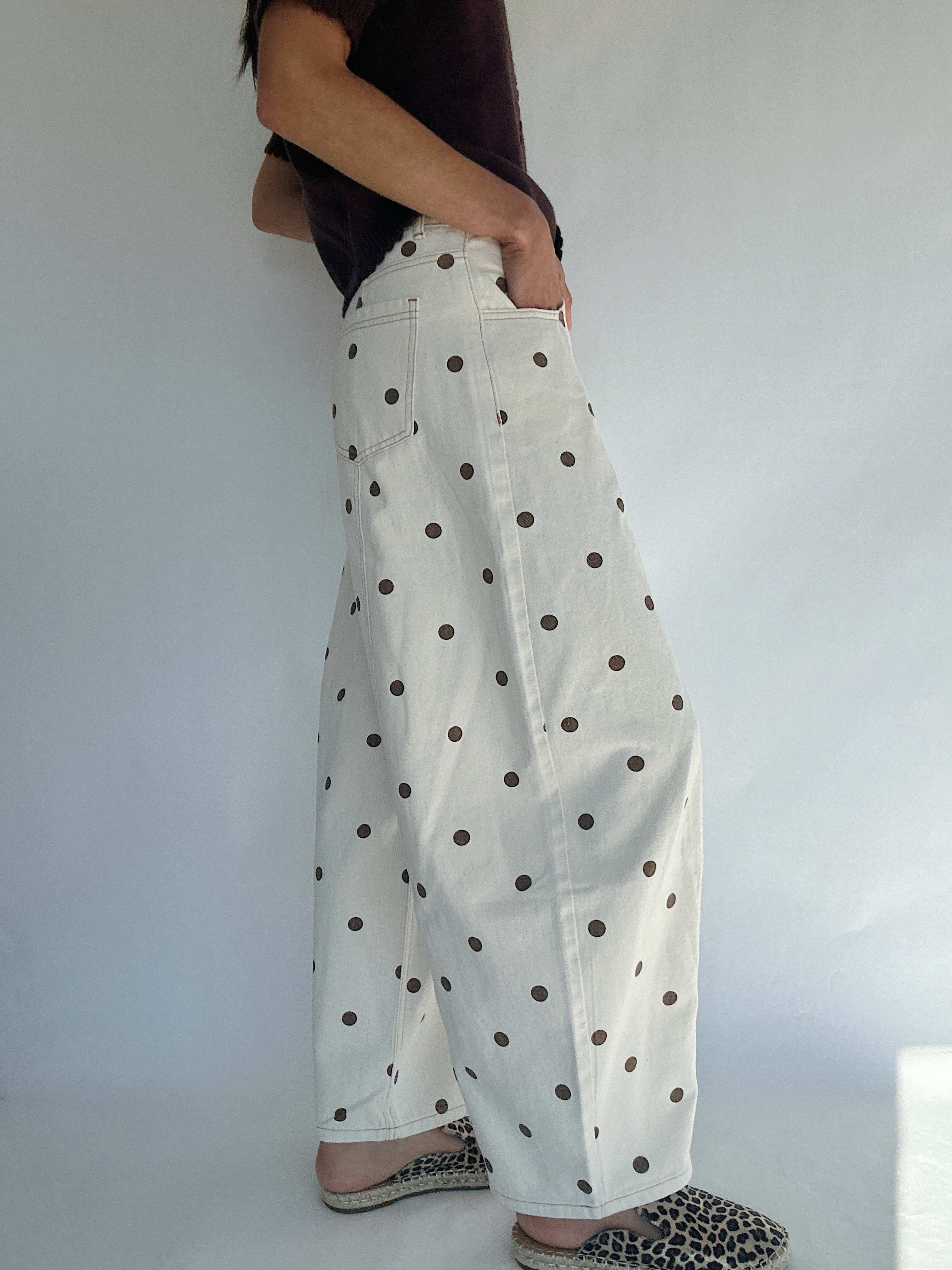 Person wearing white barrel style pants with brown polka dots against a plain background side view