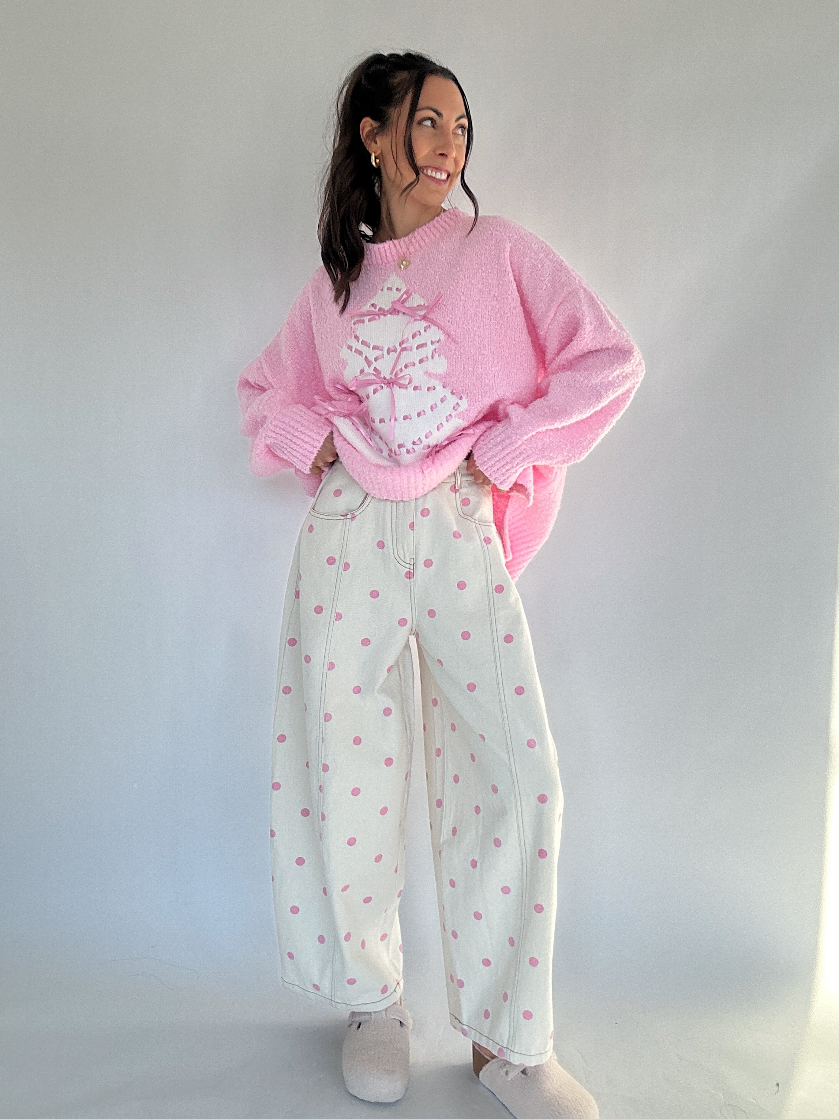 Person wearing a pink sweater and white pants with pink polka dots against a plain background