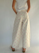 Person wearing a white top and beige pants with pink polka dots against a plain background