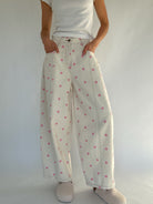 Person wearing white barrel pants with pink polka dots and a white shirt against a plain background