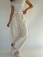 Person wearing white pants with pink polka dots and a white top against a plain background