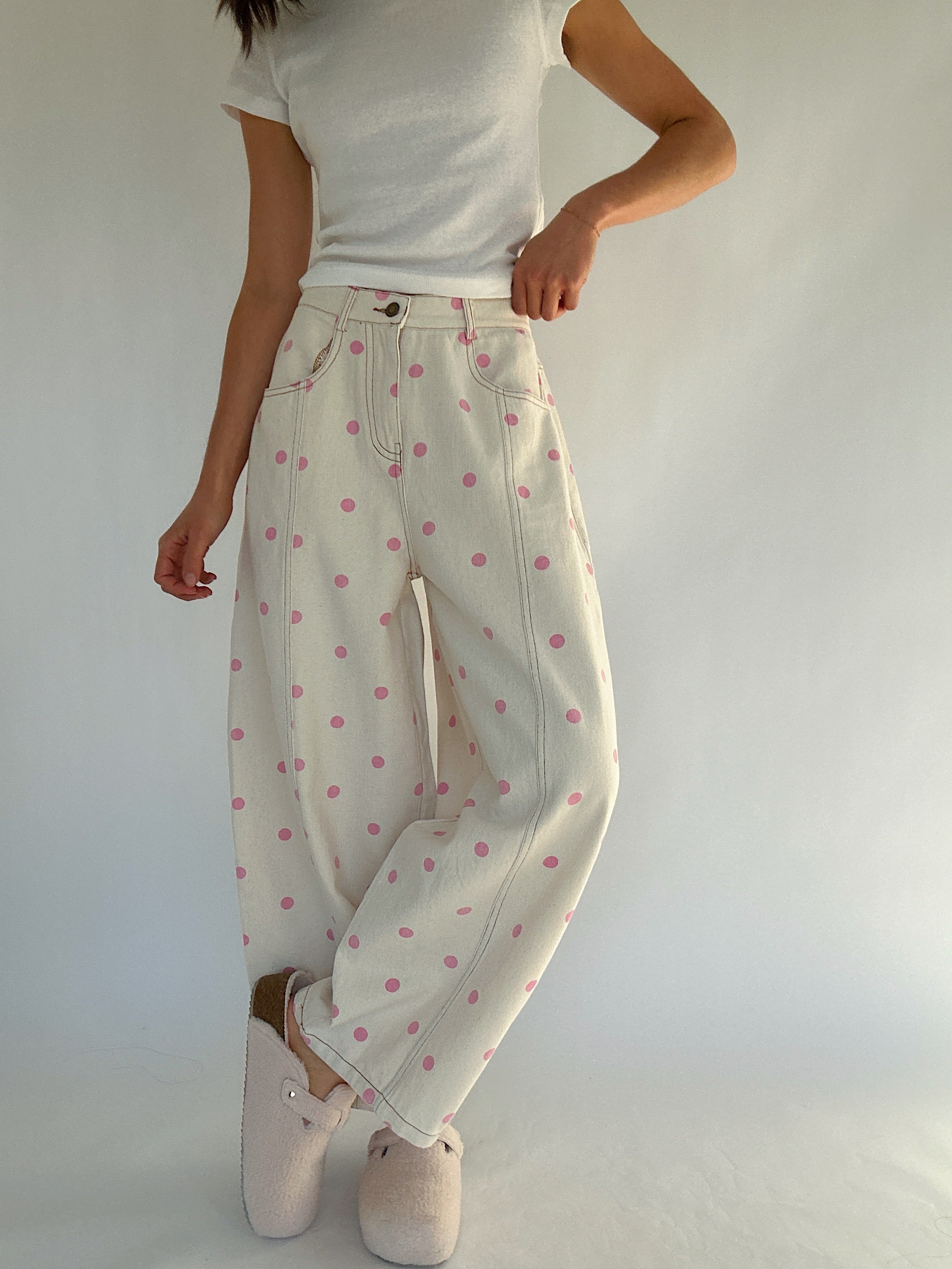 Person wearing white pants with pink polka dots and a white top against a plain background